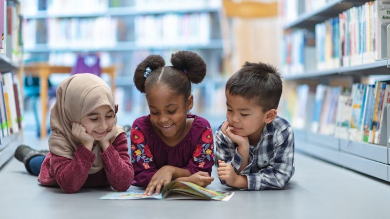 3 kids lying on the floor, looking at a book